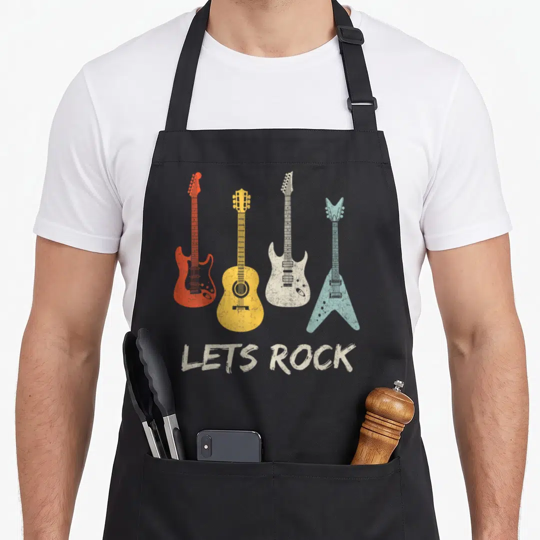 Rock roll apron - Four guitars in red, yellow, beige, and blue above LETS ROCK text — shown on a black cotton canvas apron against a white background