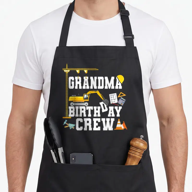 Crew grandma in apron - Excavator and construction tools surrounding stacked GRANDMA BIRTHDAY CREW text in cartoon style — shown on a black cotton canvas apron against a white background
