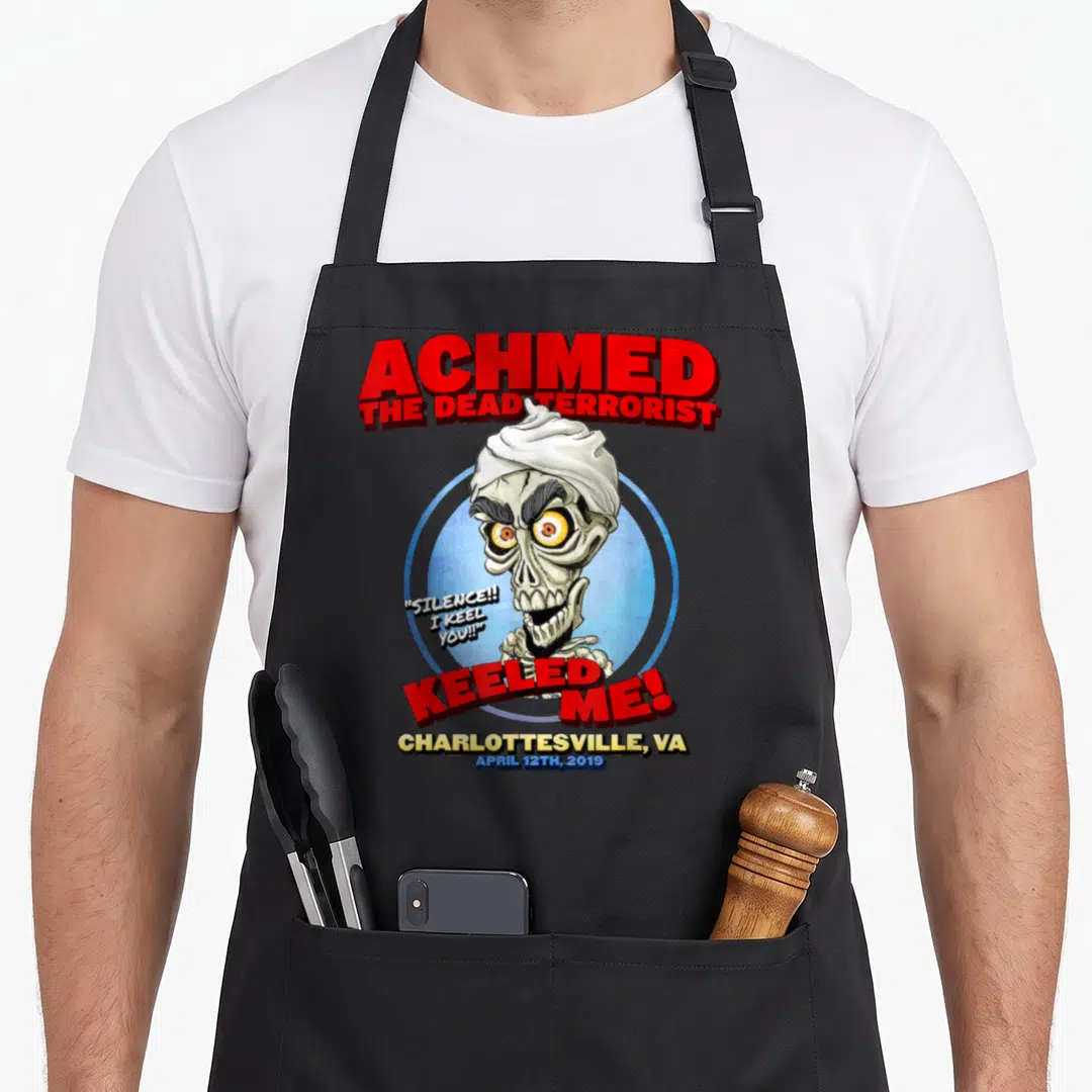 Achmed charlottesville apron - Cartoon skeleton in blue circle with red and yellow text reading keeled me — shown on a black cotton canvas apron against a white background