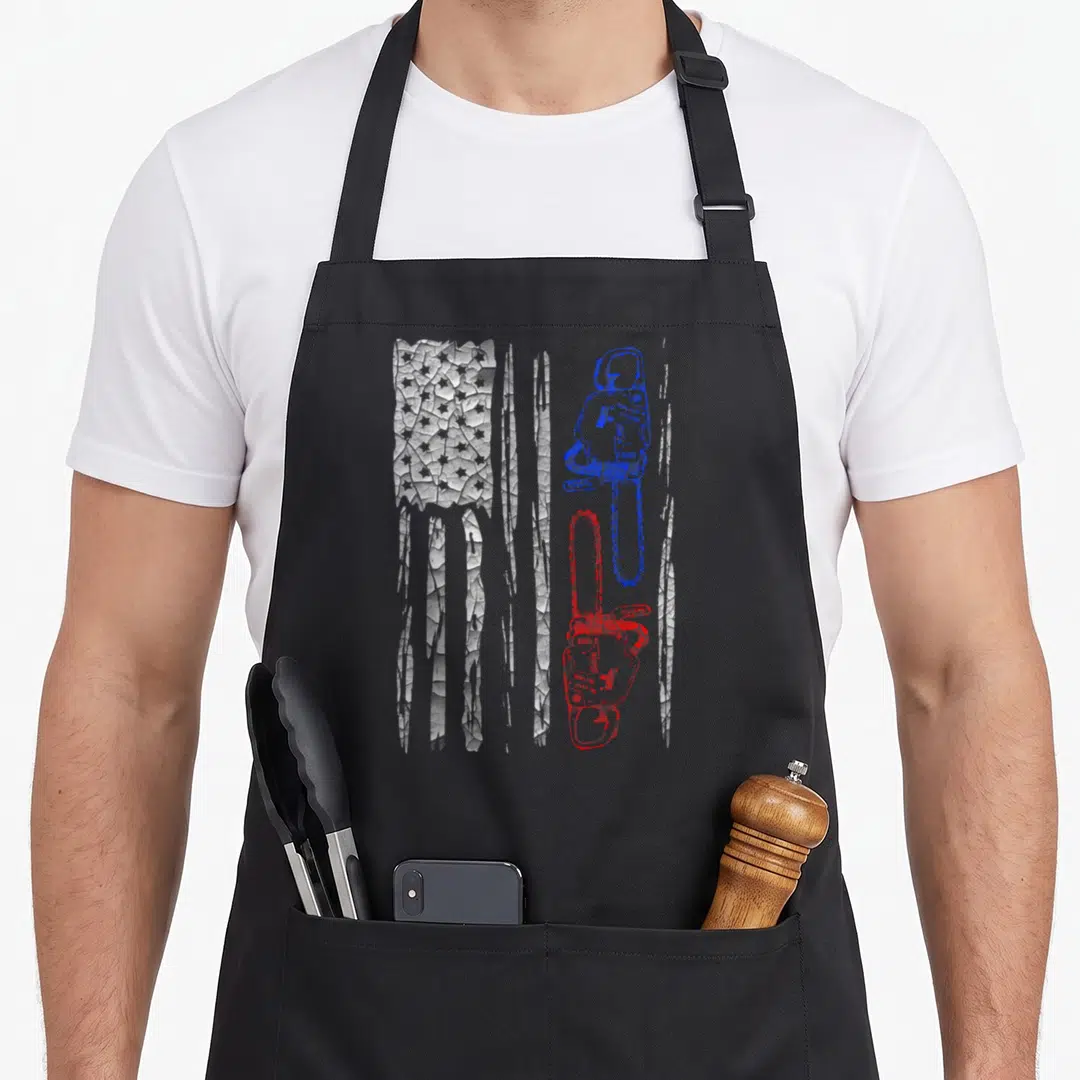 Flag chainsaw apron - Two vertical chainsaws in blue and red over a distressed white flag background — shown on a black cotton canvas apron against a white background