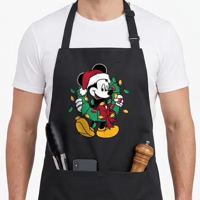 Cute christmas lights apron - Mickey Mouse in Santa hat holding a green wreath with red, green, and yellow light bulbs — shown on a black cotton canvas apron against a white background