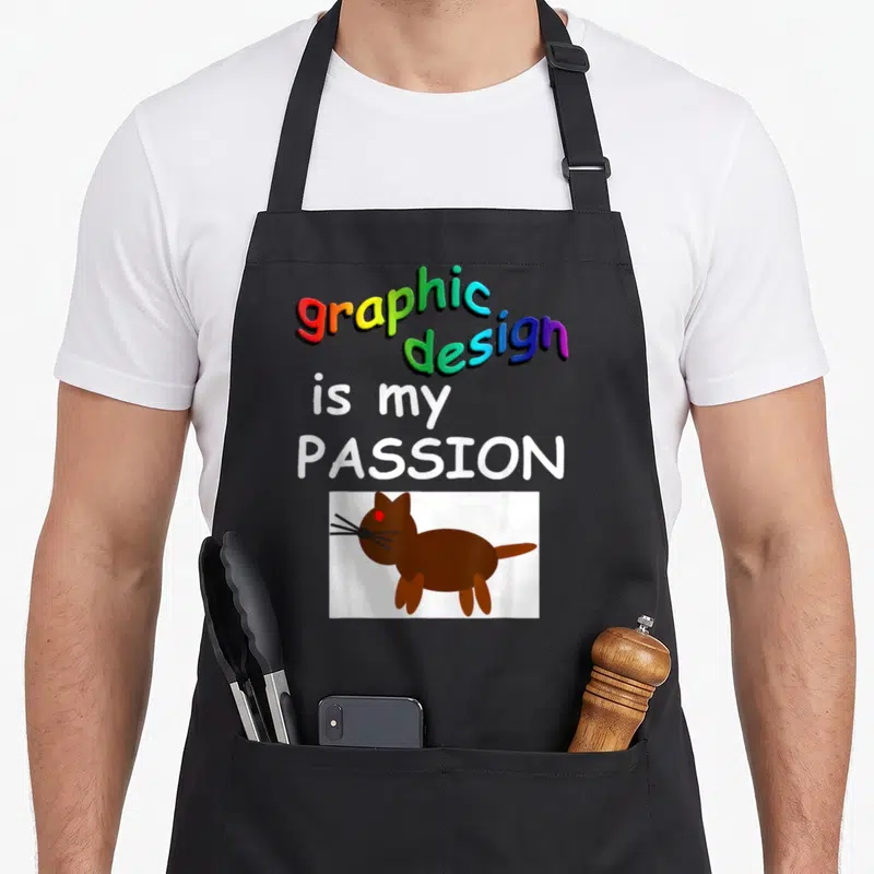 Passion illustrator apron - Rainbow text graphic design is my passion above cartoon brown cat in white box — shown on a black cotton canvas apron against a white background