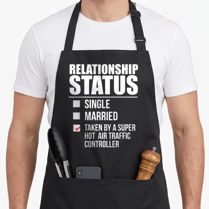 Relationship air traffic controller apron - Relationship Status checklist with red checkmark next to Taken by a Super — shown on a black cotton canvas apron against a white background