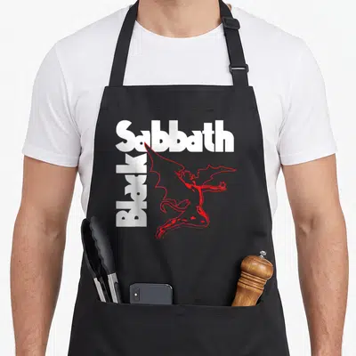 Creature black sabbath apron - White Sabbath text, vertical Black text, red winged devil holding a star — shown on a black cotton canvas apron against a white background