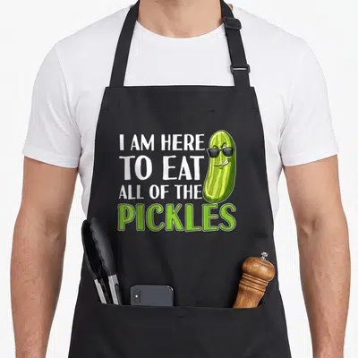 Funny eat pickle apron - Stacked text I AM HERE TO EAT ALL OF THE PICKLES next to a green cartoon pickle with black — shown on a black cotton canvas apron against a white background