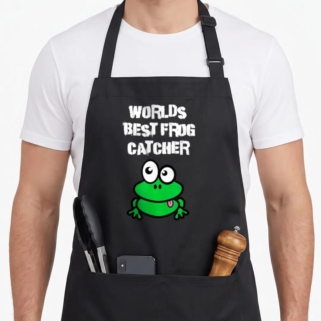 Funny catcher frog aprons - Three lines of white text reading WORLDS BEST FROG CATCHER above a green cartoon frog — shown on a black cotton canvas apron against a white background