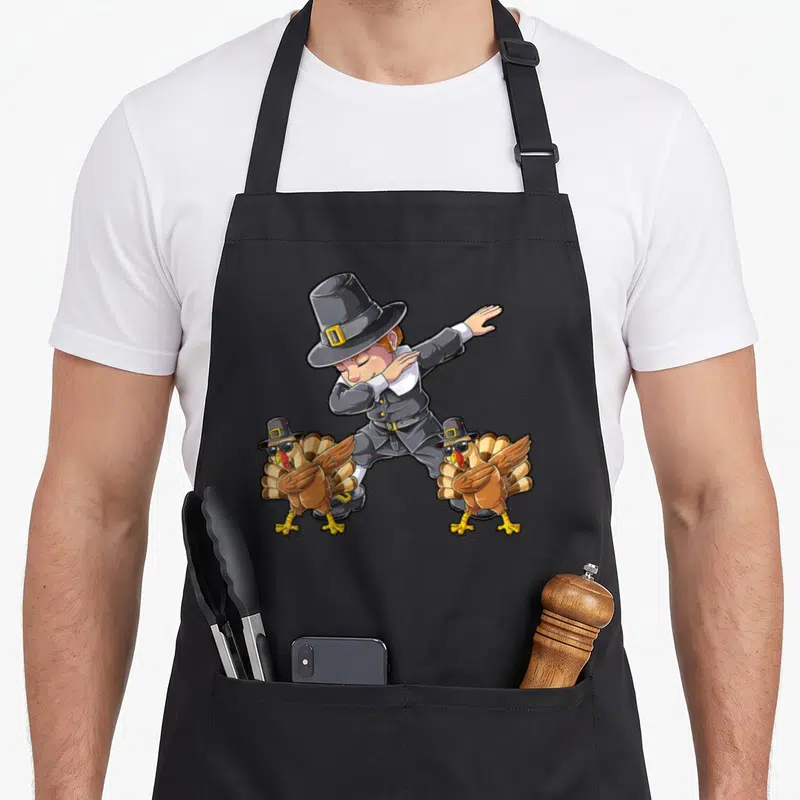Dab thanksgiving day aprons - Cartoon pilgrim dabbing flanked by two turkeys wearing hats and sunglasses on a black — shown on a black cotton canvas apron against a white background