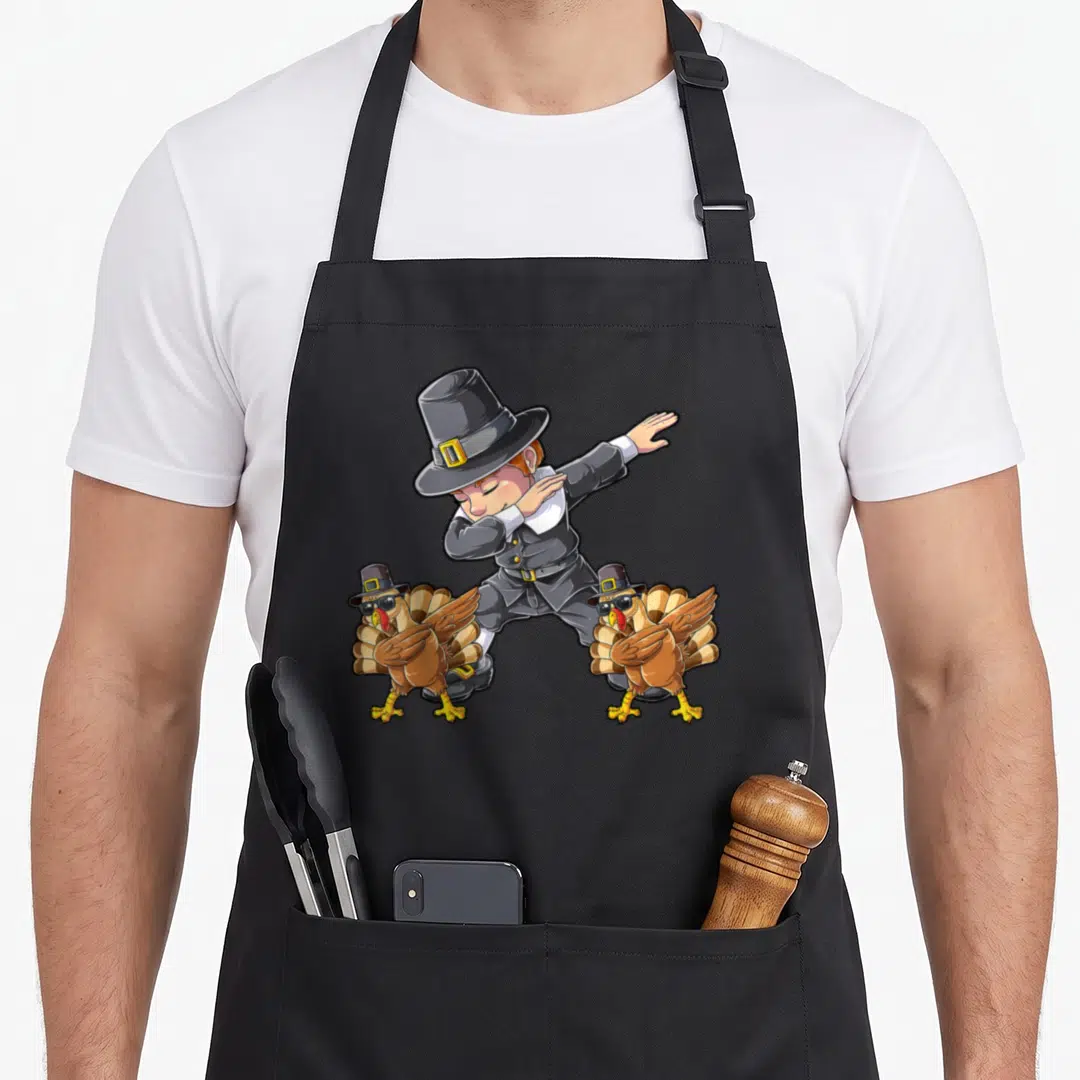 Dab thanksgiving day aprons - Cartoon pilgrim dabbing flanked by two turkeys wearing hats and sunglasses on a black — shown on a black cotton canvas apron against a white background