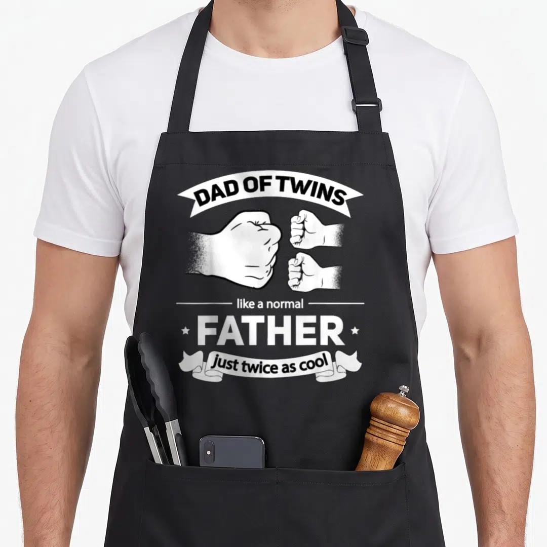 Funny twin father day apron - Dad of Twins text with one large and two small fists in black and white stacked layout — shown on a black cotton canvas apron against a white background