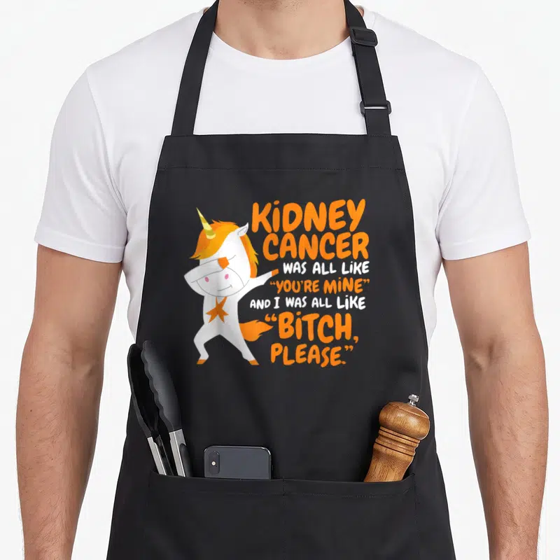 Kidney unicorn apron - White cartoon unicorn dabbing next to orange and white sarcasm text about kidney cancer survival — shown on a black cotton canvas apron against a white background
