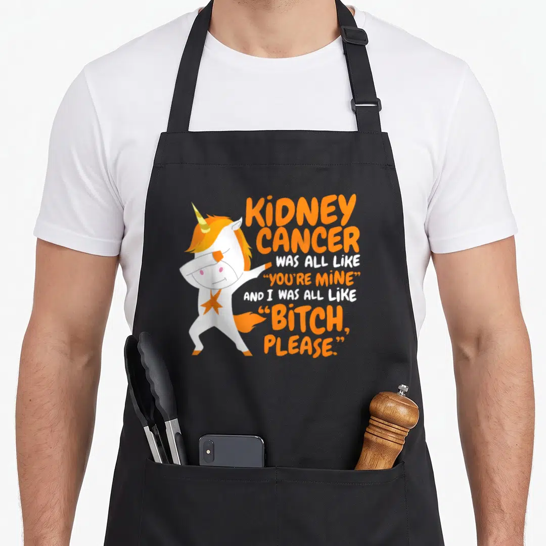 Kidney unicorn apron - White cartoon unicorn dabbing next to orange and white sarcasm text about kidney cancer survival — shown on a black cotton canvas apron against a white background