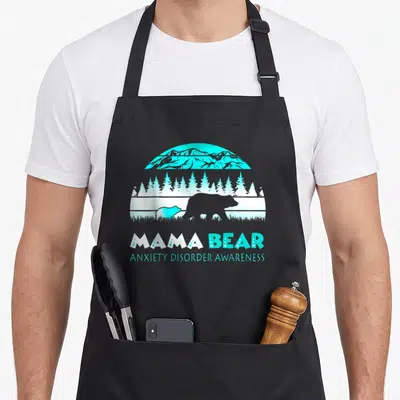 Anxiety mama bear apron - Cyan and white bear silhouette landscape with MAMA BEAR ANXIETY DISORDER AWARENESS text — shown on a black cotton canvas apron against a white background