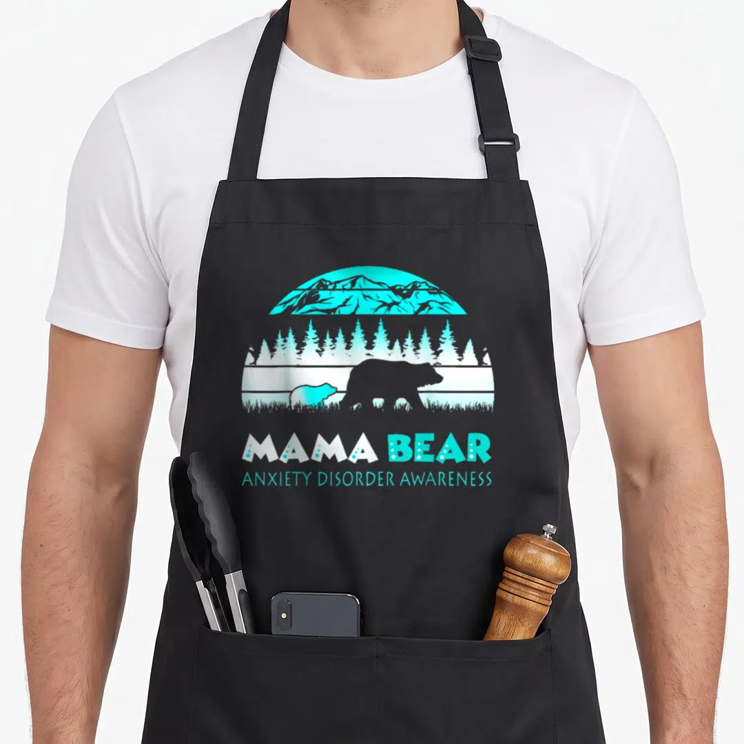 Anxiety mama bear apron - Cyan and white bear silhouette landscape with MAMA BEAR ANXIETY DISORDER AWARENESS text — shown on a black cotton canvas apron against a white background