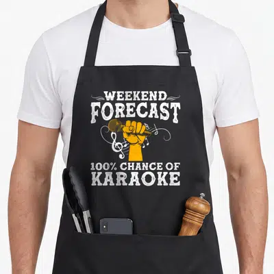 Karaoke box apron - Distressed white text Weekend Forecast 100% Chance of Karaoke above orange hand holding microphone — shown on a black cotton canvas apron against a white background