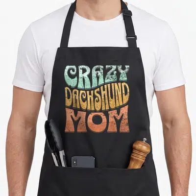 Dachshund apron for mom - Stacked retro text reading Crazy Dachshund Mom in mint yellow and coral — shown on a black cotton canvas apron against a white background