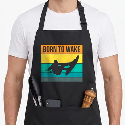 Wake wakeboarding apron - Grey wakeboarder silhouette over orange yellow teal and grey stripes with BORN TO WAKE text — shown on a black cotton canvas apron against a white background