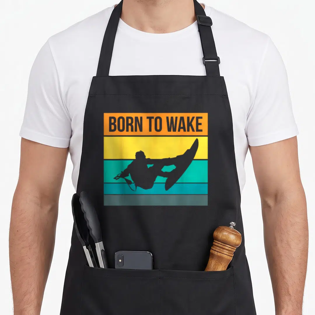 Wake wakeboarding apron - Grey wakeboarder silhouette over orange yellow teal and grey stripes with BORN TO WAKE text — shown on a black cotton canvas apron against a white background