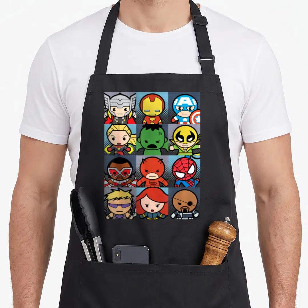 Boxed kawaii apron - Twelve superhero cartoon figures in red blue yellow green 4x3 grid squares — shown on a black cotton canvas apron against a white background