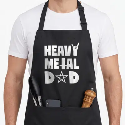Concert heavy metal apron - White stacked text HEAVY METAL DAD with hand and star symbols on black fabric — shown on a black cotton canvas apron against a white background