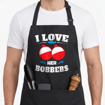Bobber fishing apron - I Love Her Bobbers text with two red white bobbers and blue fish illustration — shown on a black cotton canvas apron against a white background