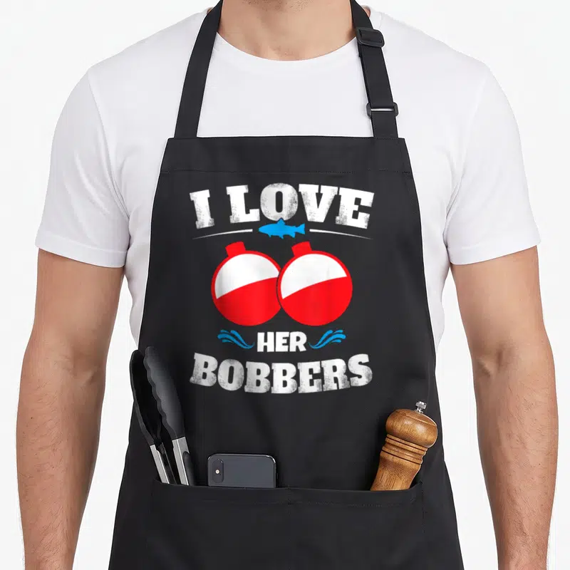 Bobber fishing apron - I Love Her Bobbers text with two red white bobbers and blue fish illustration — shown on a black cotton canvas apron against a white background