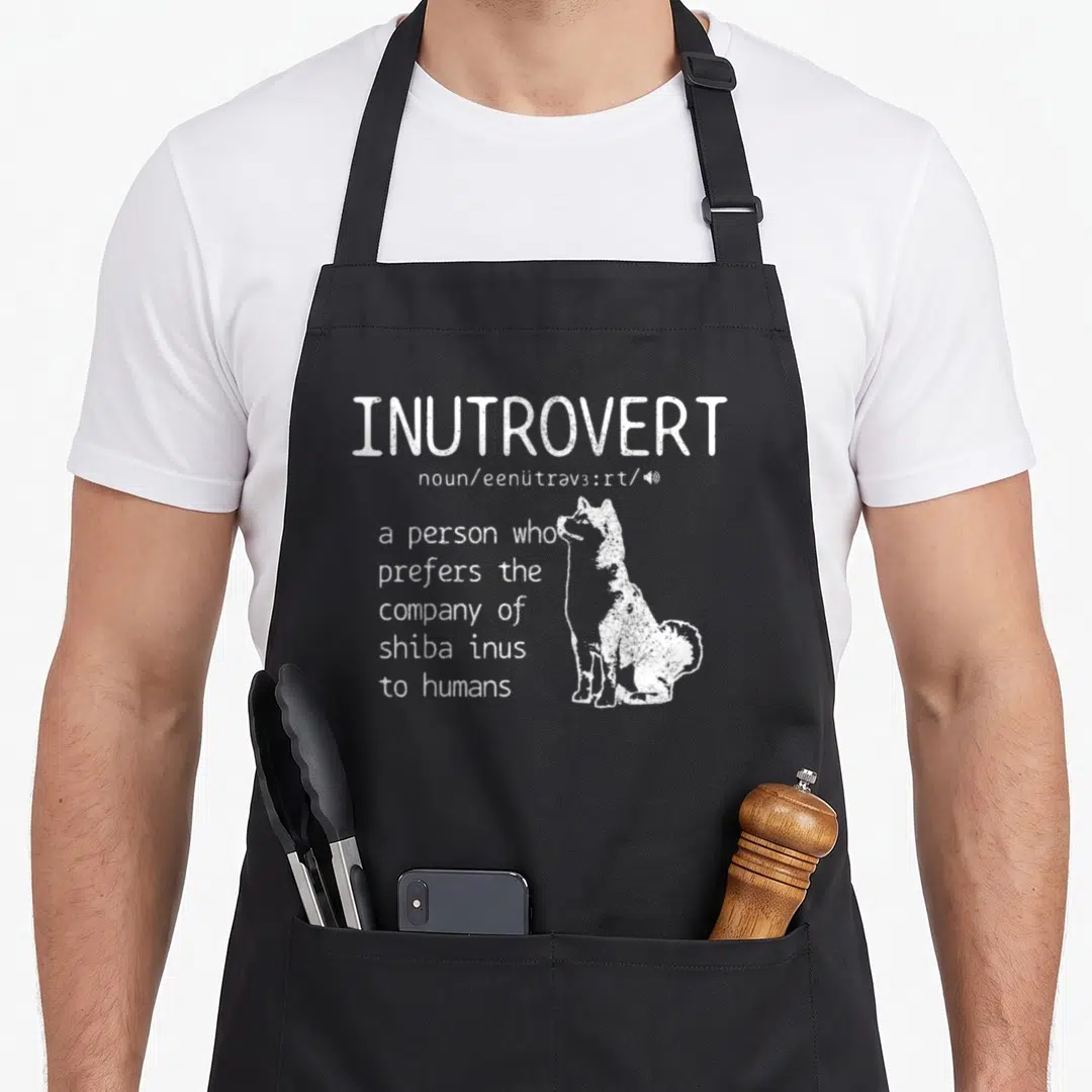 Inutrovert dog apron - White INUTROVERT definition text next to sitting shiba inu silhouette — shown on a black cotton canvas apron against a white background