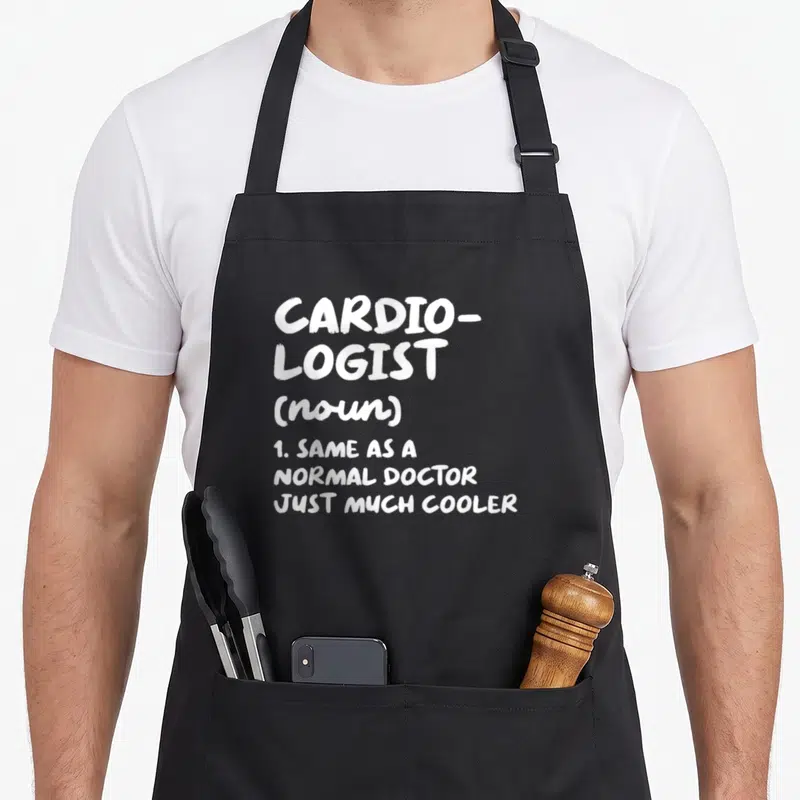 Cardiologist doctor apron - White stacked text defining cardiologist as a cooler version of a normal doctor — shown on a black cotton canvas apron against a white background