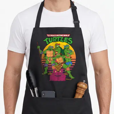 Sun teenage cooking aprons - Four turtles and a rat sitting cross-legged in front of a yellow striped circle — shown on a black cotton canvas apron against a white background