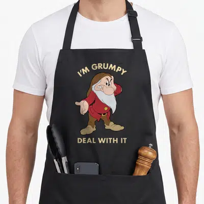Deal snow white apron - Cartoon dwarf in red coat with text I'M GRUMPY DEAL WITH IT arched above and straight below — shown on a black cotton canvas apron against a white background