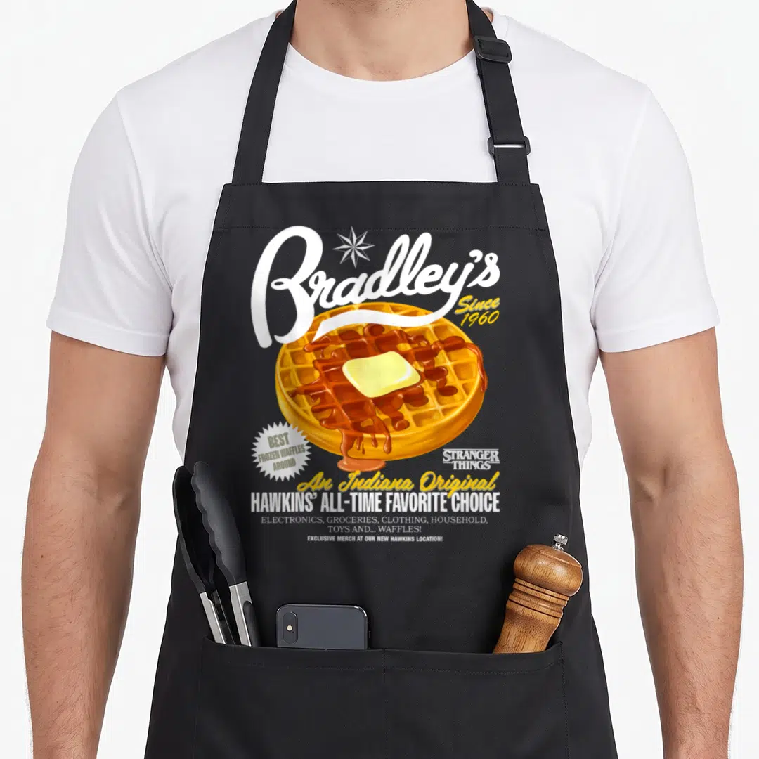Season frozen apron - Retro waffle with butter and syrup under white Bradley's script and yellow Indiana Original text — shown on a black cotton canvas apron against a white background