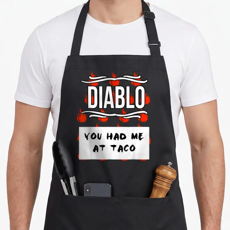Sauce halloween apron - DIABLO text with red flames and YOU HAD ME AT TACO banner — shown on a black cotton canvas apron against a white background