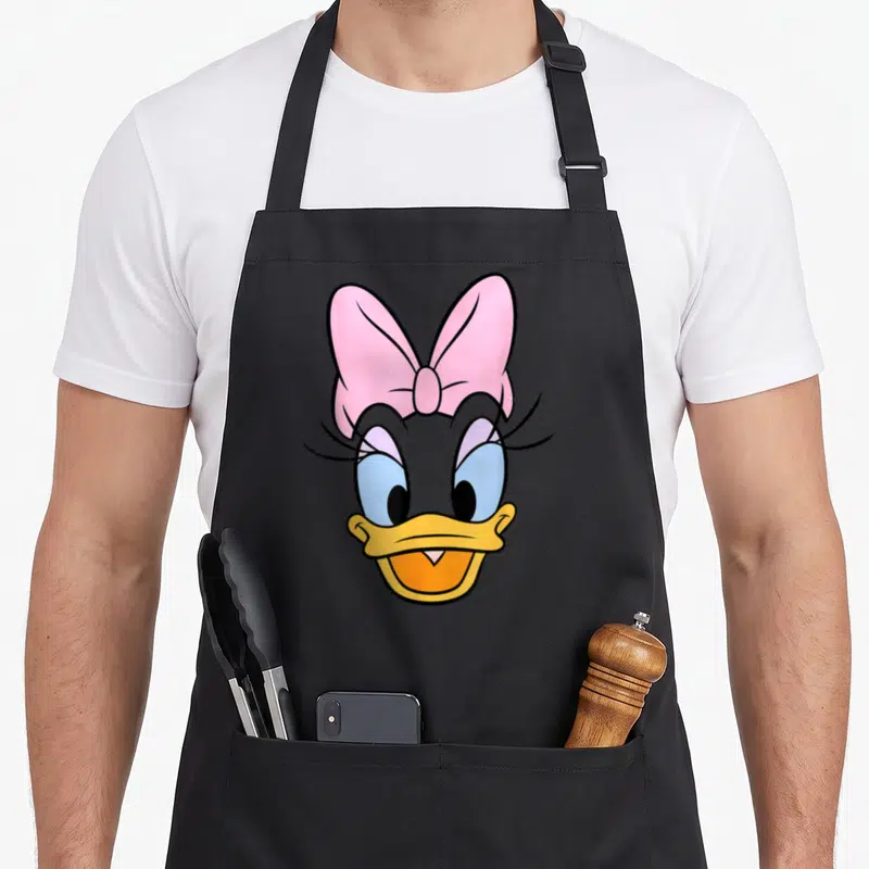 Face daisy apron - Cartoon duck head with pink bow, blue eyes, and yellow beak on grey background — shown on a black cotton canvas apron against a white background