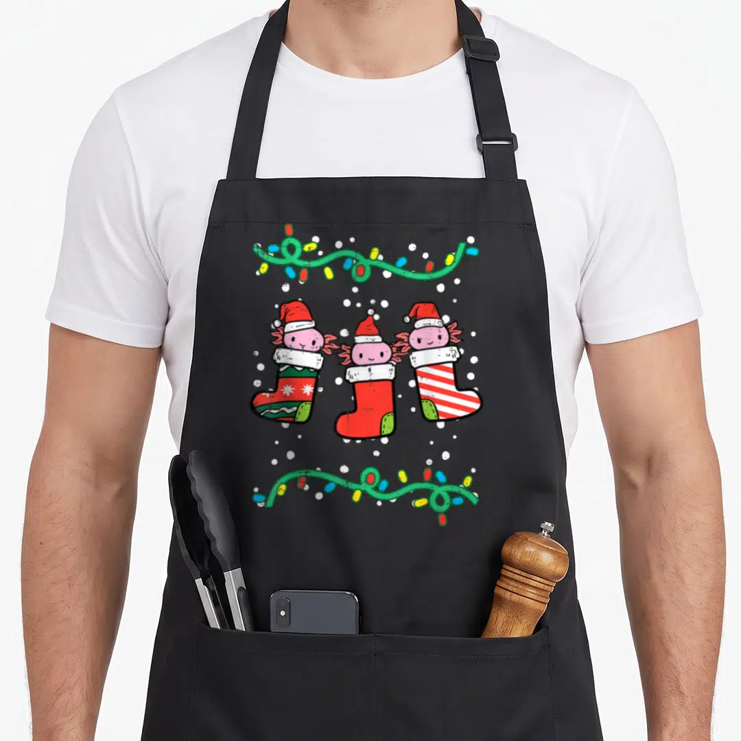 Axolotl womens christmas aprons - Three pink axolotls in Christmas stockings with string lights and snowflakes — shown on a black cotton canvas apron against a white background
