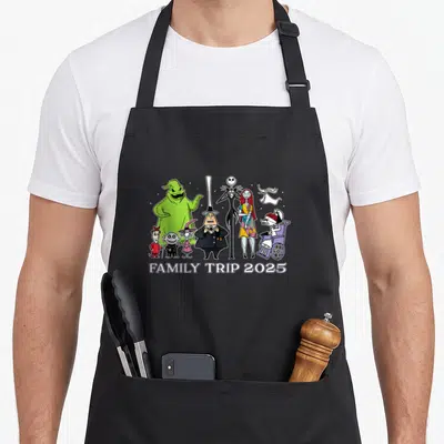 Star family aprons - Cartoon characters from The Nightmare Before Christmas in a row above FAMILY TRIP 2025 text — shown on a black cotton canvas apron against a white background