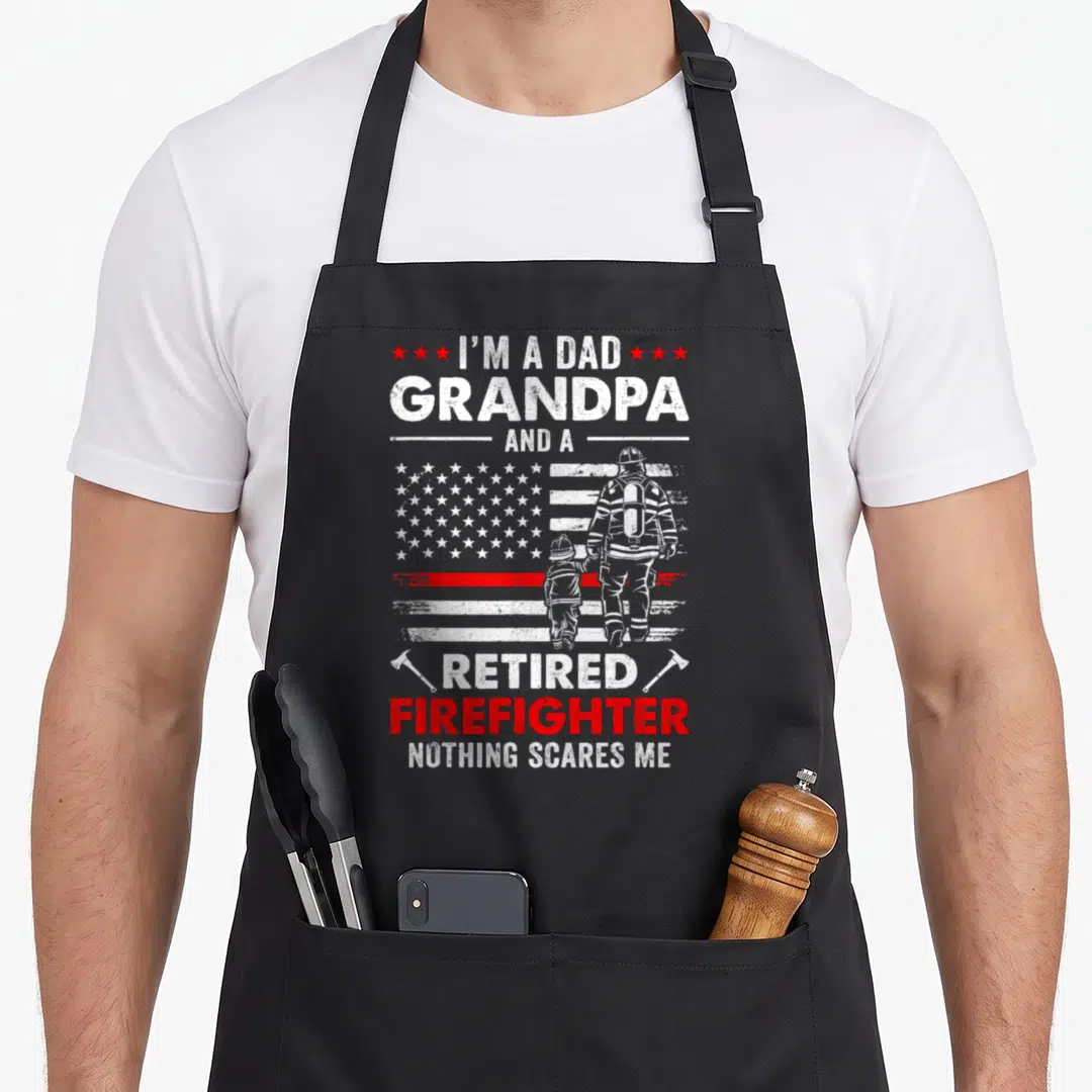 Father firefighter cooking apron - Distressed flag with firefighter and child from behind, stacked text about dad — shown on a black cotton canvas apron against a white background