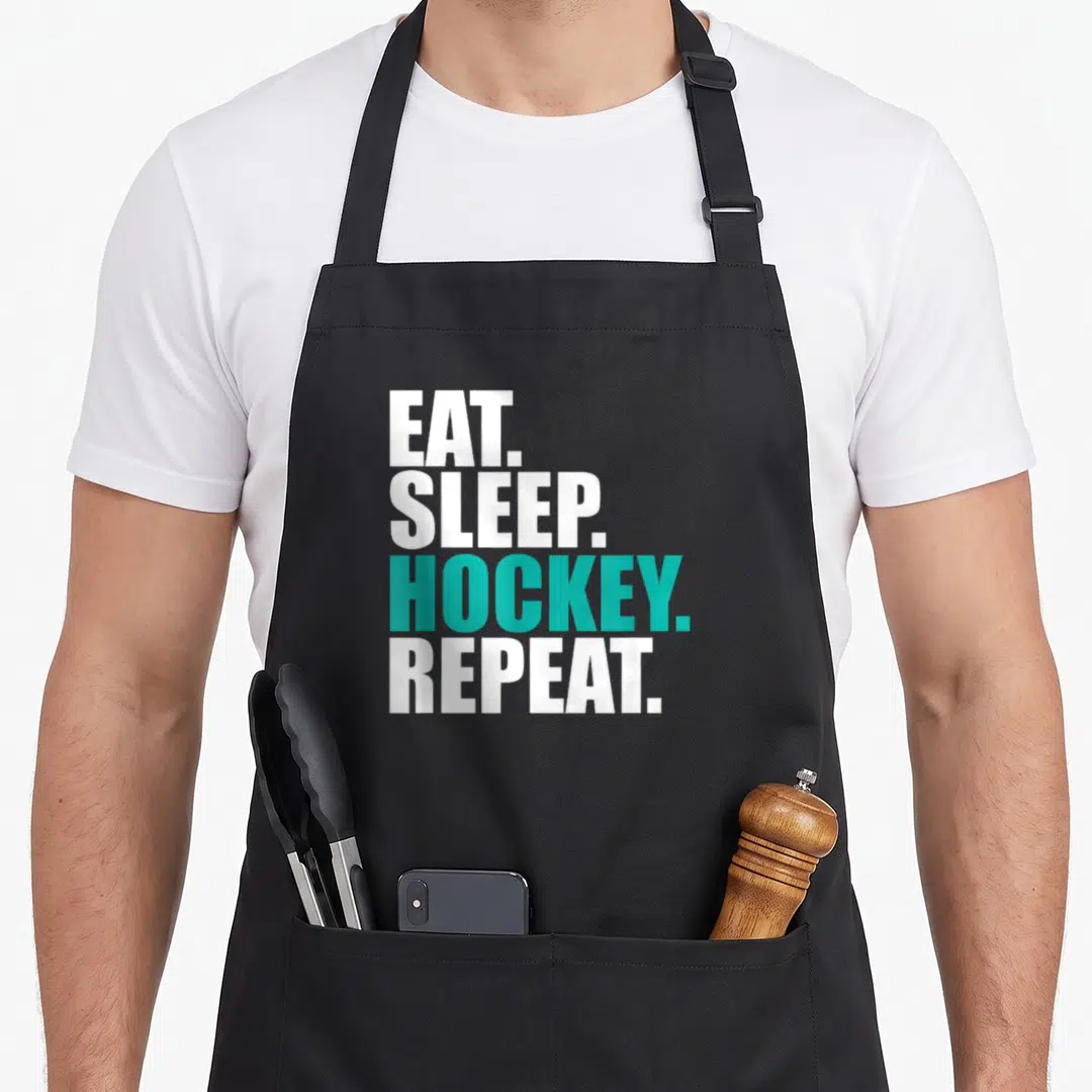 Eat hockey dad apron - Stacked white and teal text reading EAT SLEEP HOCKEY REPEAT on black fabric — shown on a black cotton canvas apron against a white background