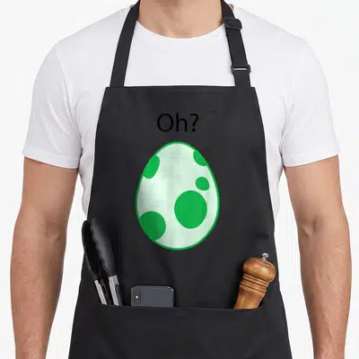 Gamer egg apron - Spotted green egg with Oh? text above in cartoon style — shown on a black cotton canvas apron against a white background