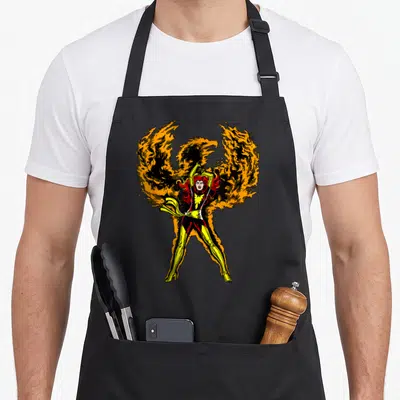 Phoenix x apron - Cartoon woman in yellow red costume with large orange fire wings behind — shown on a black cotton canvas apron against a white background