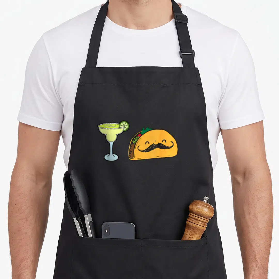 Lime mexican apron - Cartoon taco with mustache and margarita glass with lime slice in yellow blue and green — shown on a black cotton canvas apron against a white background