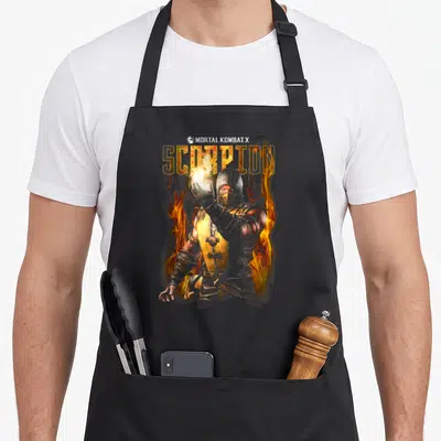 Scorpion x apron - Realistic masked ninja character below SCORPION text filled with yellow and orange fire — shown on a black cotton canvas apron against a white background