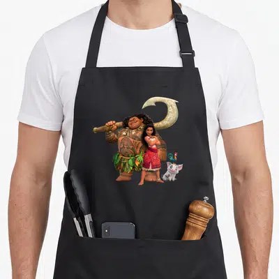 Pua novelty apron - Maui holding fishhook behind Moana with Pua pig and Heihei rooster in cartoon style — shown on a black cotton canvas apron against a white background