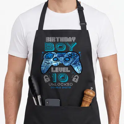Unlocked double birthday apron - Blue marbled game controller with BOY 10 DOUBLE DIGITS text and stars — shown on a black cotton canvas apron against a white background