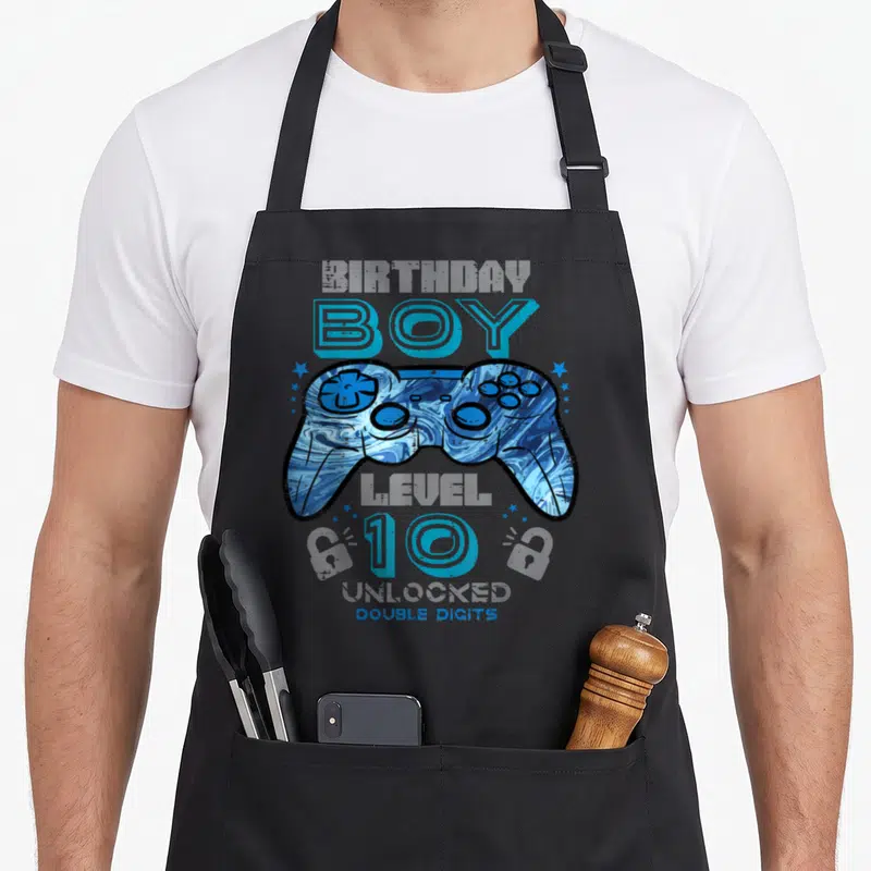 Unlocked double birthday apron - Blue marbled game controller with BOY 10 DOUBLE DIGITS text and stars — shown on a black cotton canvas apron against a white background