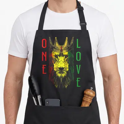 Rasta african apron - Crowned lion head with vertical ONE LOVE text in red yellow green distressed print — shown on a black cotton canvas apron against a white background