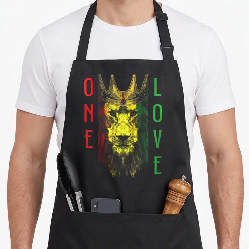 Rasta african apron - Crowned lion head with vertical ONE LOVE text in red yellow green distressed print — shown on a black cotton canvas apron against a white background