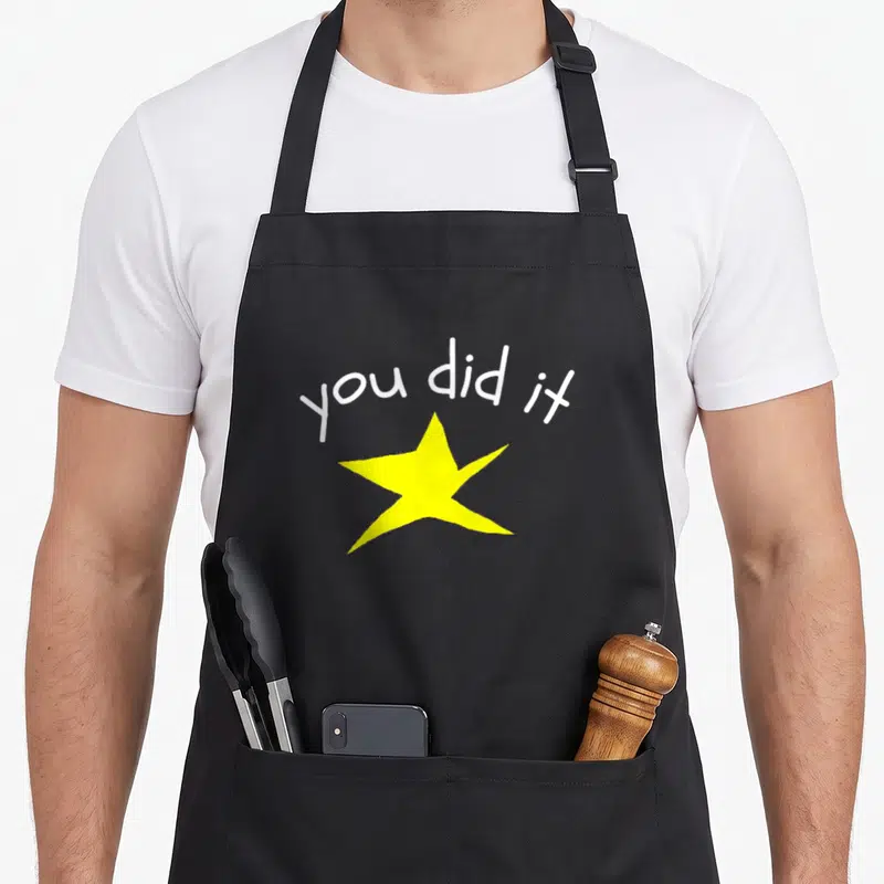 School valedictorian humor apron - White you did it text arched over a large yellow star — shown on a black cotton canvas apron against a white background
