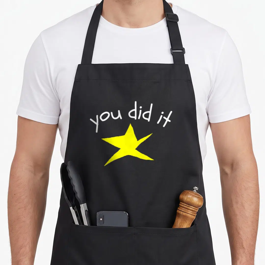 School valedictorian humor apron - White you did it text arched over a large yellow star — shown on a black cotton canvas apron against a white background