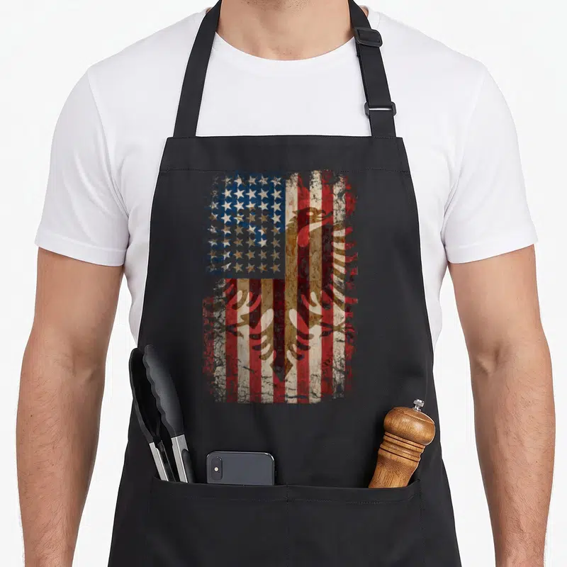 Albania root american flag apron - Distressed brown eagle superimposed over weathered red white and blue stars — shown on a black cotton canvas apron against a white background