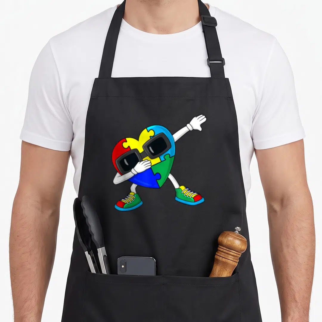 Dabbing pull girl apron - Cartoon heart made of red yellow blue green and white puzzle pieces wearing sunglasses — shown on a black cotton canvas apron against a white background