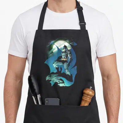 Glow glowing apron - Realistic Batman standing before a moon with a gargoyle at his feet in blue and grey — shown on a black cotton canvas apron against a white background